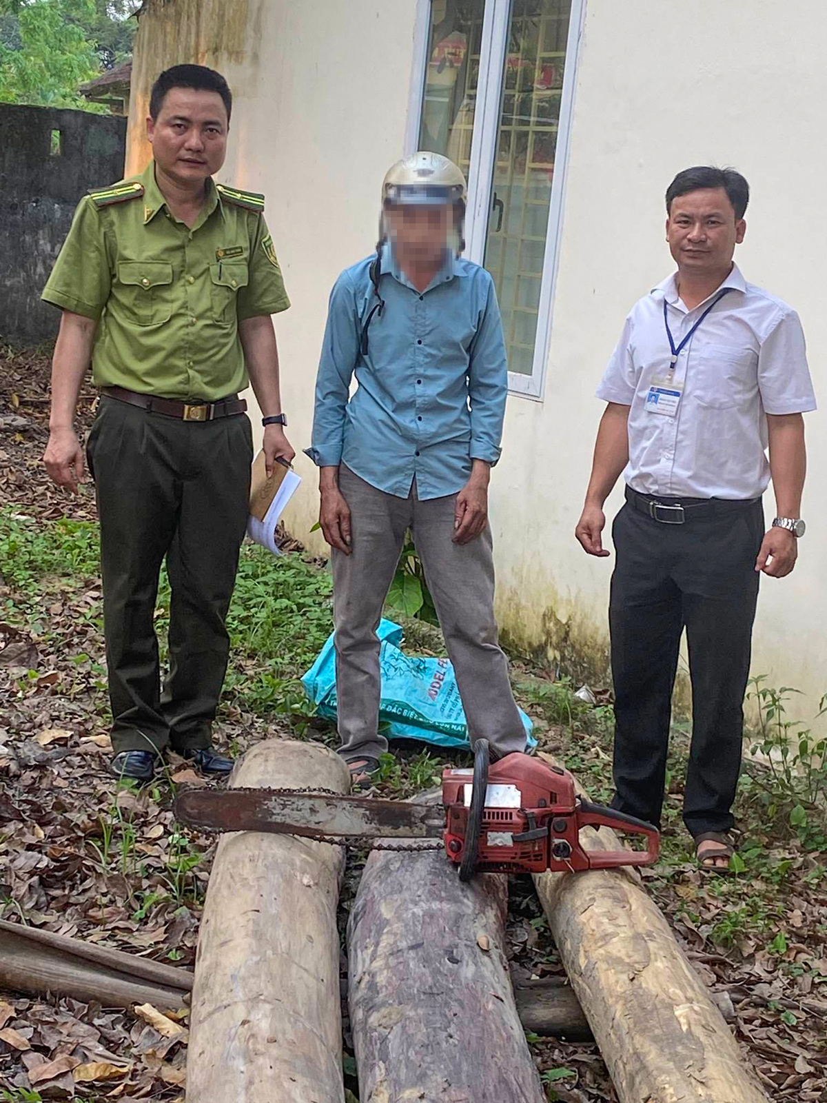 Đối tượng H.V.V (đứng giữa) và công cụ cưa xăng dùng cắt cây gỗ trái phép tại UBND xã Thanh Hà.